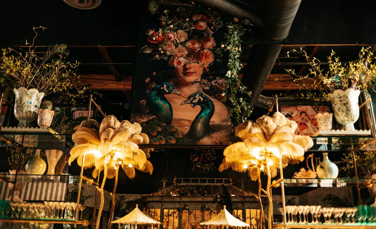 A luxuriously styled event space with golden feather lamps and a vibrant peacock mural, illustrating the importance of atmosphere in event planning by Gather Catering in San Diego.